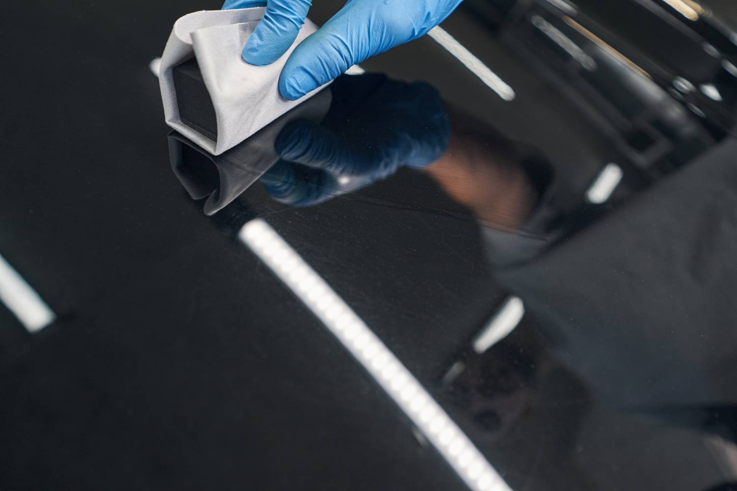 Close up of man applying ceramic coating on black car at detailing service