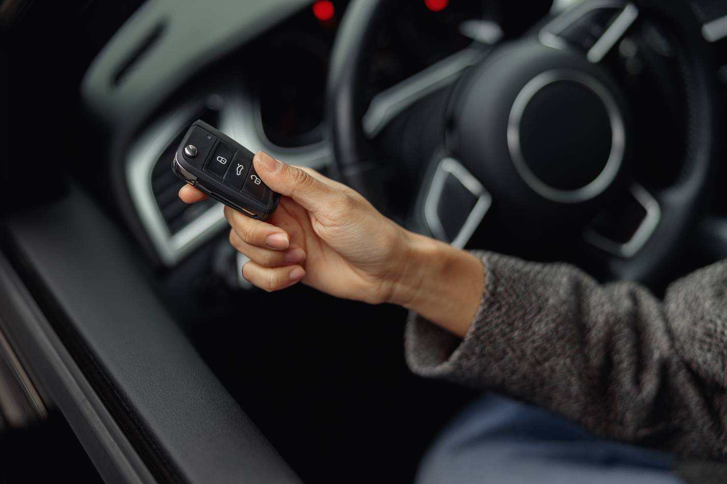 Close up of woman hand holding keys sitting in her new car in dealership. High quality photo
