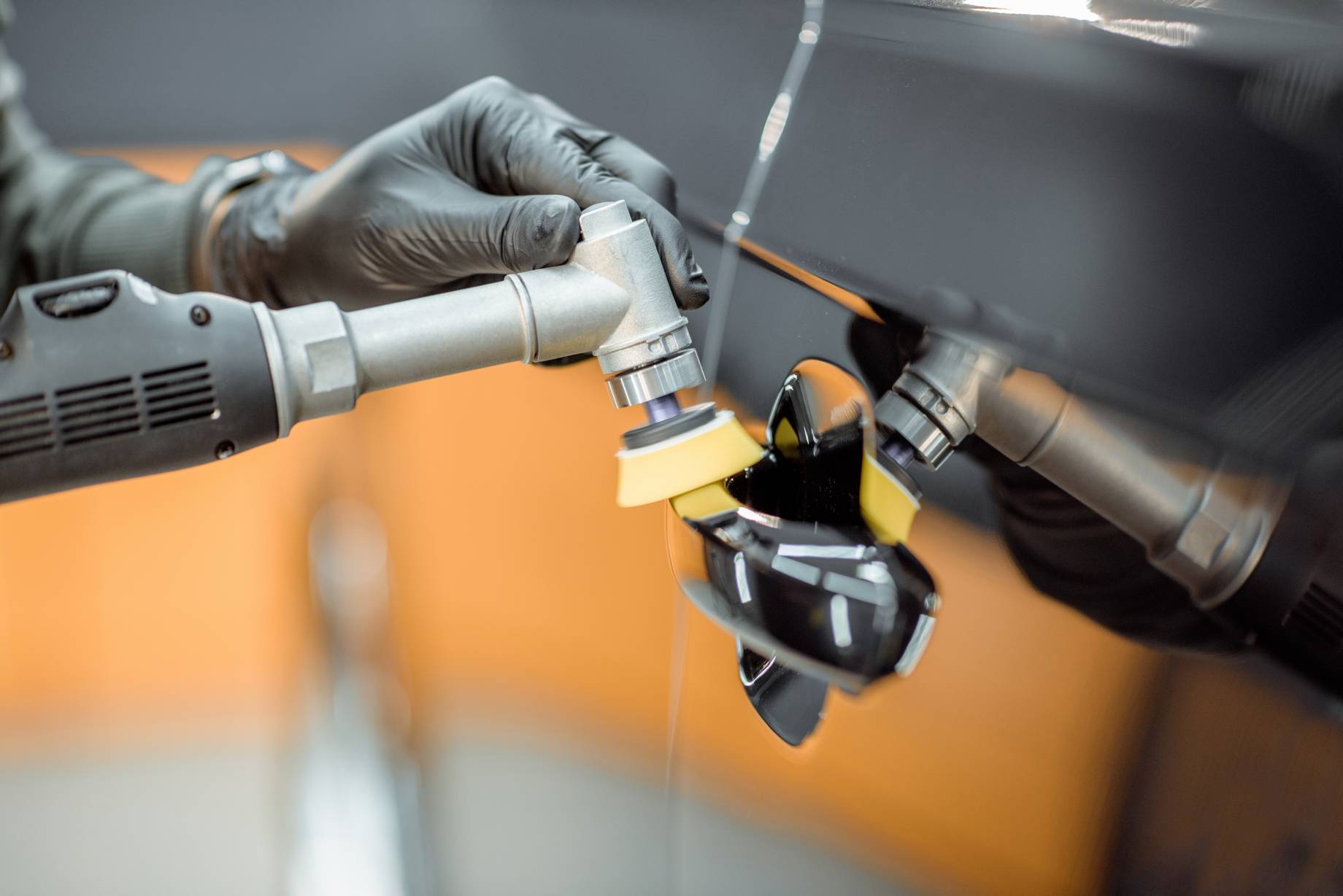 Car service worker polishing vehicle door handle with special wax from scratches, close-up. Professional car detailing and maintenance concept