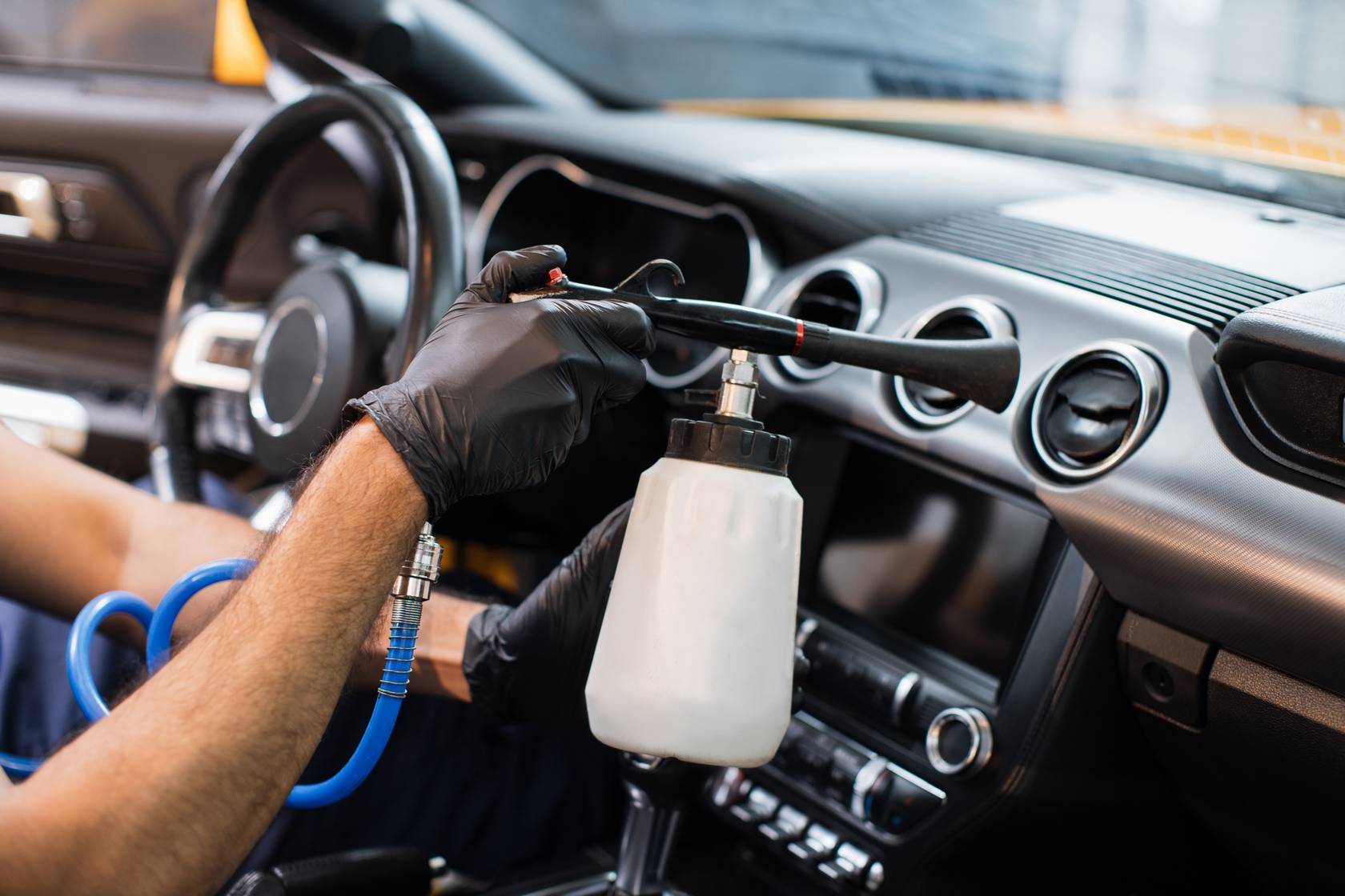 Car wash service. Close up of hands of male worker cleaning automobile salon with air gun. Professional chemical cleaning of vehicle interior with air gun machine.